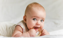 Six-month baby girl on her stomach with teether in the mouth